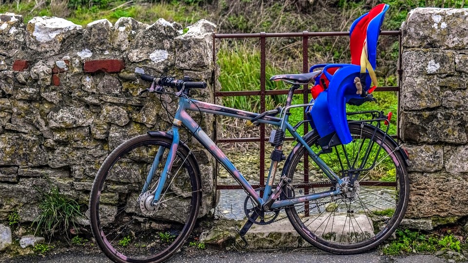 Rodzinne wycieczki rowerowe to nie tylko świetny sposób na aktywne spędzanie czasu, ale również budowanie wspólnych wspomnień, fot. Pixabay Rower z zamontowanym fotelikiem rowerowym, oparty o kamienny mur, obok metalowa furtka.