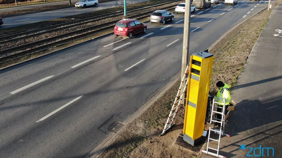 Sznur samochodów na ul. Hetmańskiej. Na poboczu trwa montaż fotoradaru.