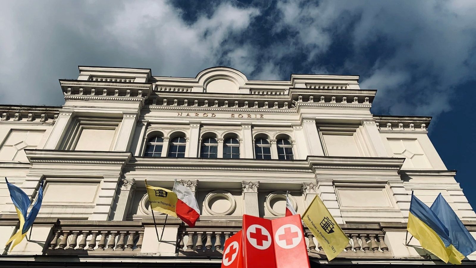 Zdjęcie przedstawia ukraińskie, niebiesko-żółte flagi powiewające na Teatrze Polskim.