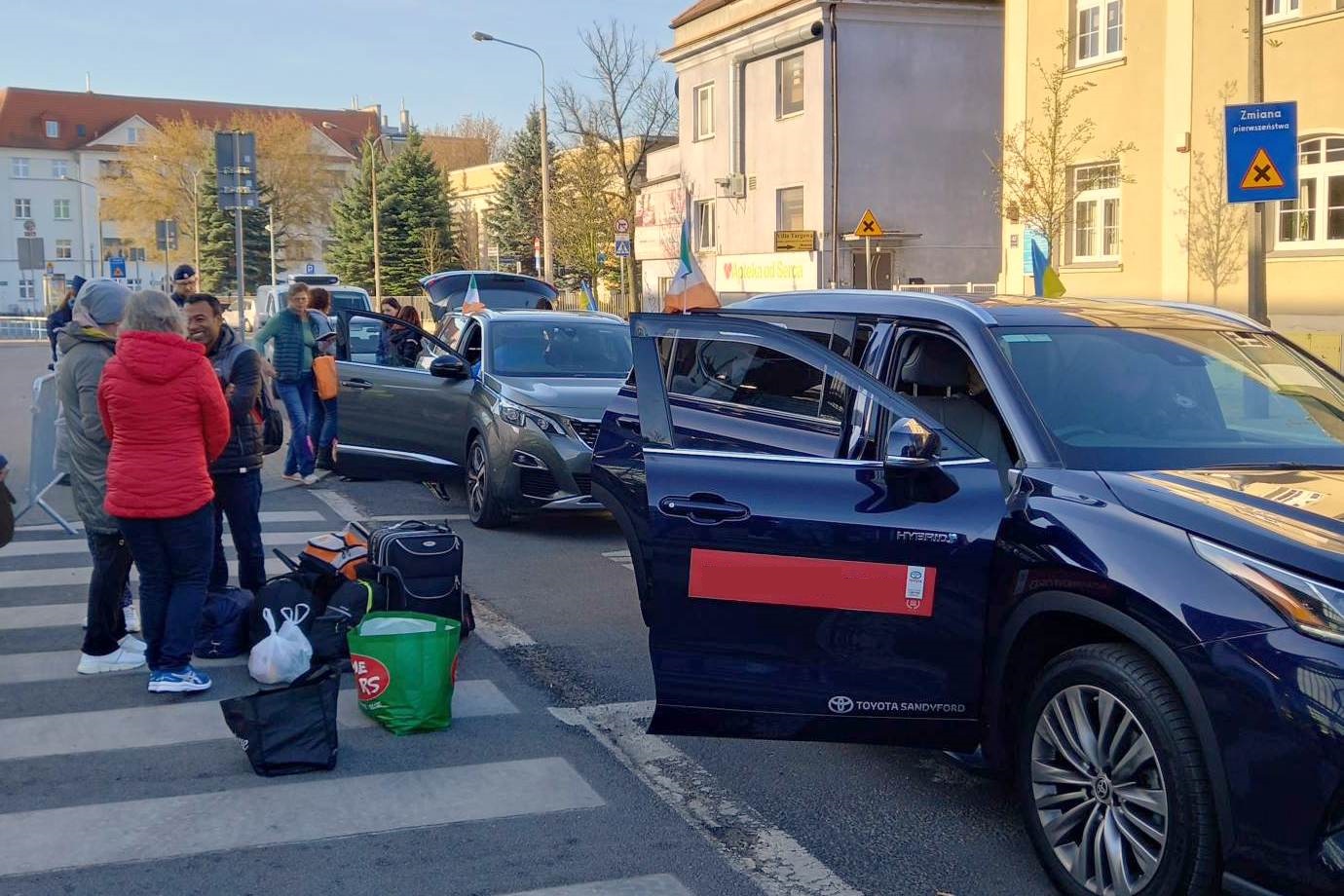 Na zdjęciu grupa ludzi z bagażami wchodzi do rzędu zaparkowanych samochodów - grafika artykułu