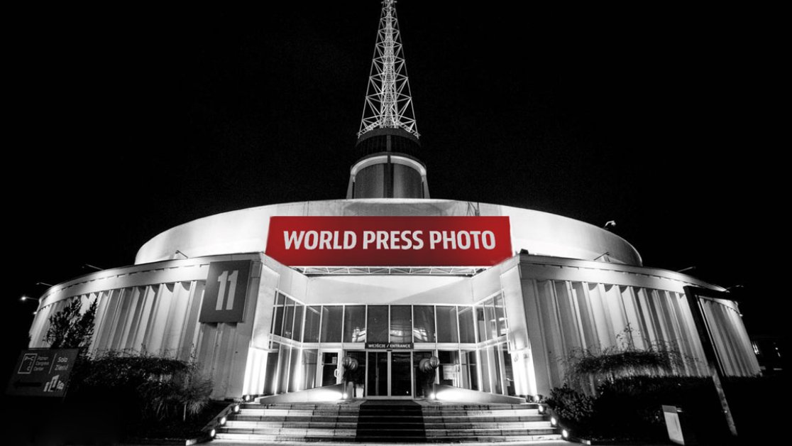 Grafika przedstawia zdjęcie budynku Iglicy MTP z napisem "World Press Foto". Fotografia jest czarno-biała, kolorowy jest tylko napis.