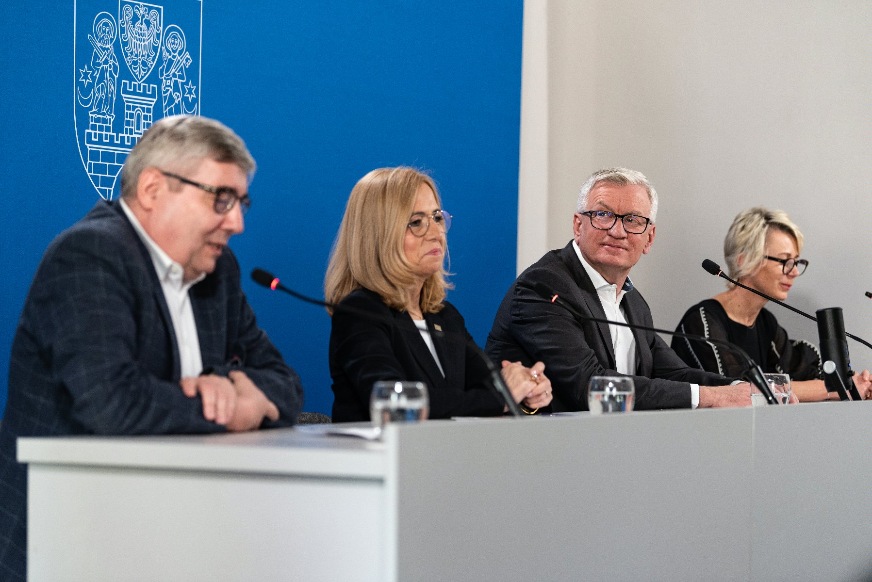 Na zdjęciu cztery osoby za stołem konferencyjnym, w środku prezydent Poznania, w tle granatowa ścianka - grafika artykułu