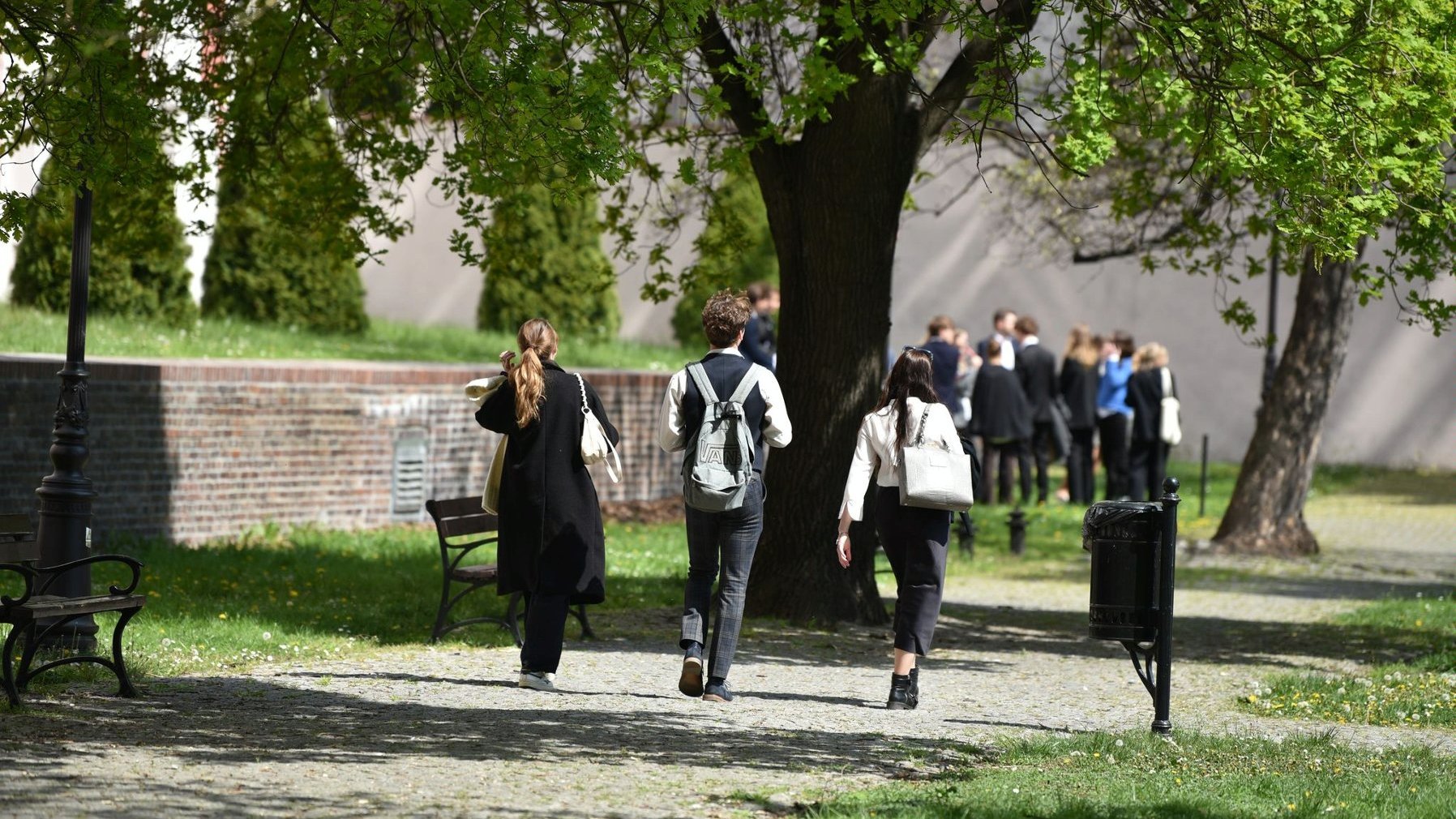 Na zdjęciu grupa młodych ludzi ubrana oficjalnie idzie przez park