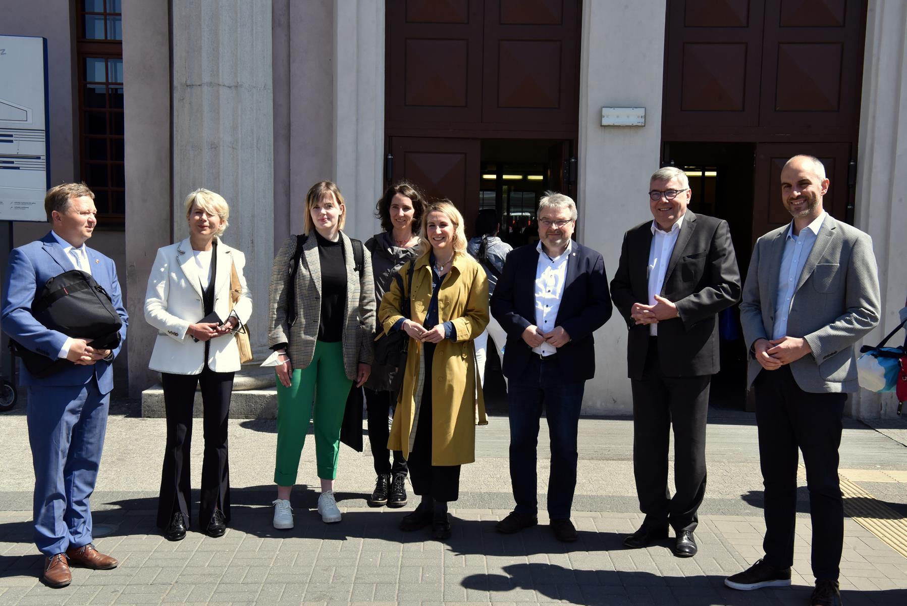 Na zdjęciu delegacja - grupa ludzi stojących obok siebie, za nimi budynek dworca - grafika artykułu