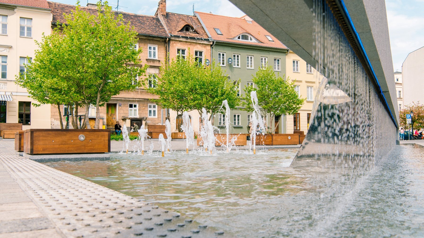 Na zdjęciu plac Kolegiacki, na pierwszym planie fontanna, w tle drzewa