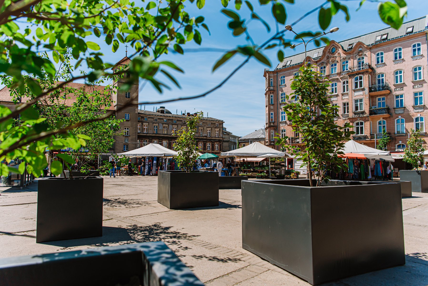 Galeria zdjęć przedstawia plac Bernardyński. Widać na nich donice z roślinami oraz stragany handlowe. - grafika artykułu