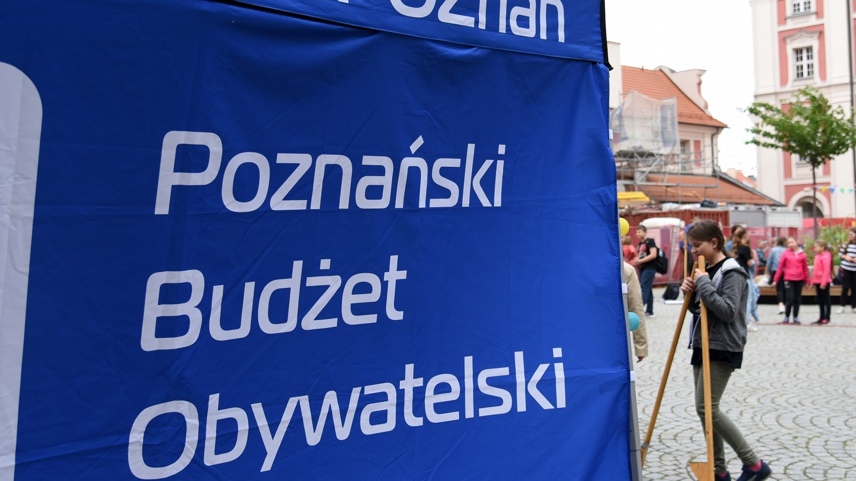 Zdjęcie przedstawia namiot z napisem "Poznański Budżet Obywatelski". W tle widać bawiące się dzieci.