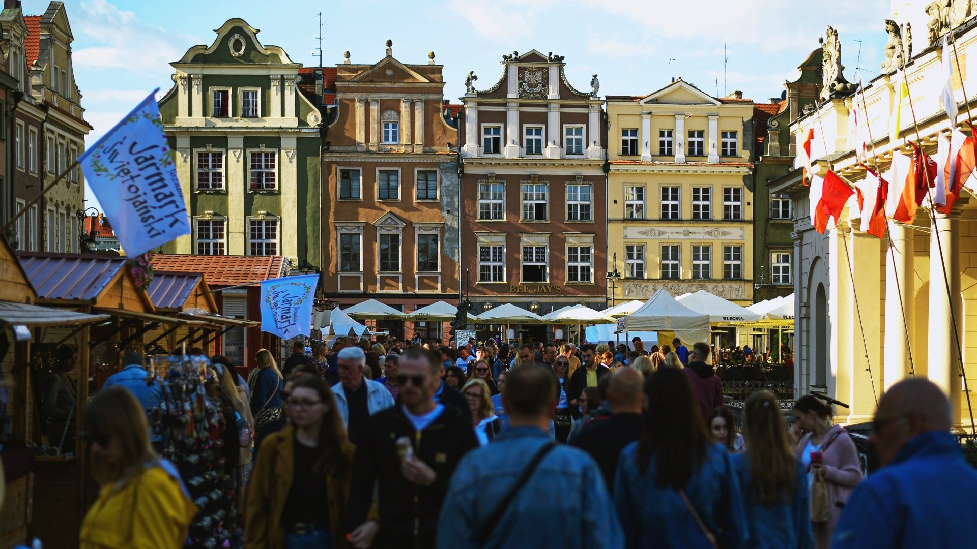 Galeria zdjęć przedstawia tłum ludzi na rynku podczas jarmarku i drewniane domki i stragany z różnymi towarami.