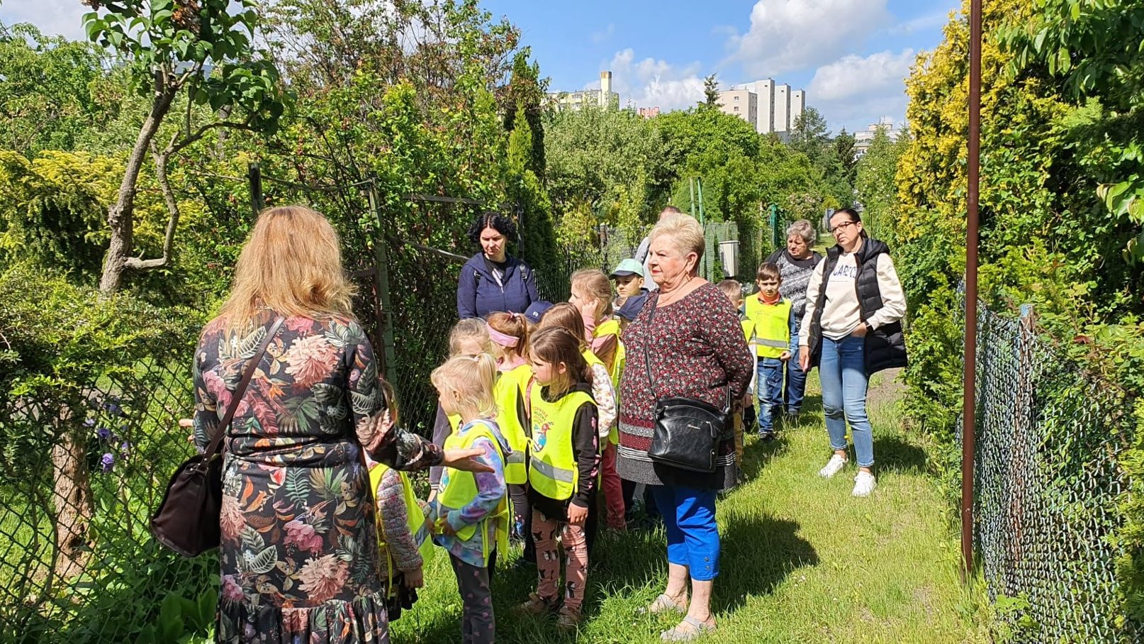 Zdjęcie przedstawia dzieci i ich opiekunów w ogrodzie.