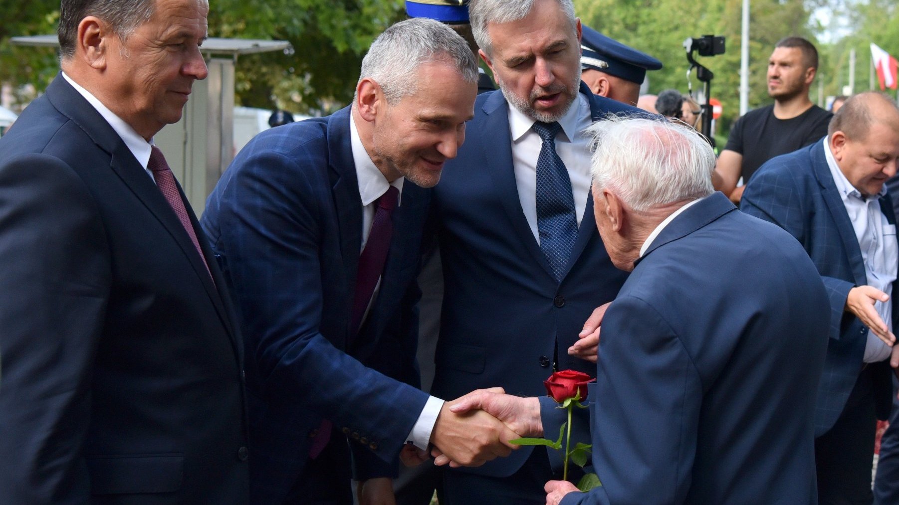 Na zdjęciu czterej mężczyźni w garniturach, witają się nawzajem