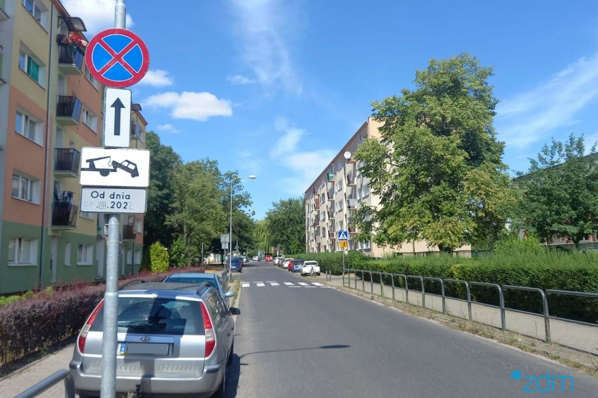 Na zdjęciu ulica, przy niej zaparkowane samochody. Na pierwszym planie znak informujący o tym, że trzeba przeparkować auta - grafika artykułu