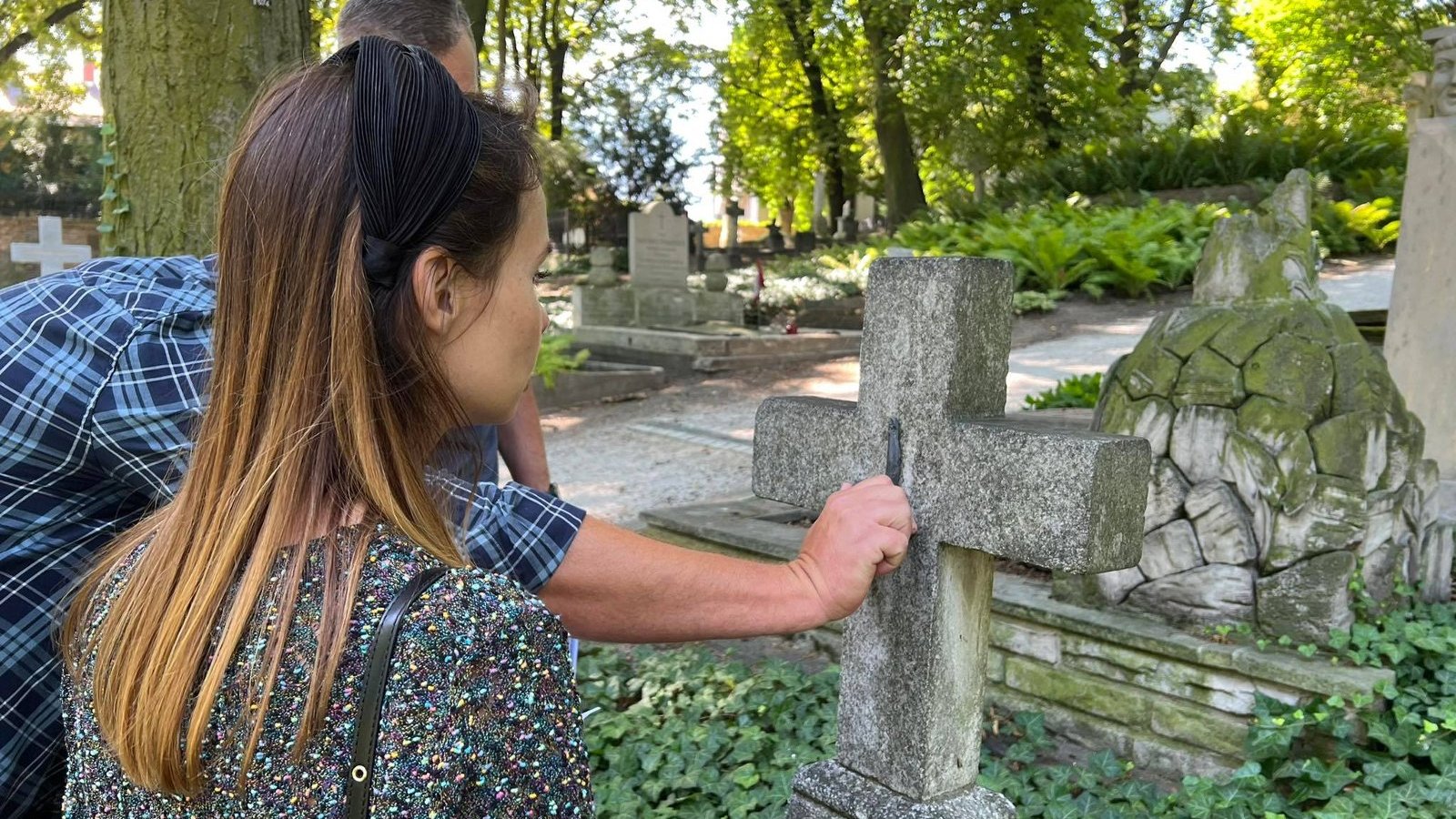 Galeria zdjęć przedstawia nagrobki i grupę ludzi, która je ogląda.