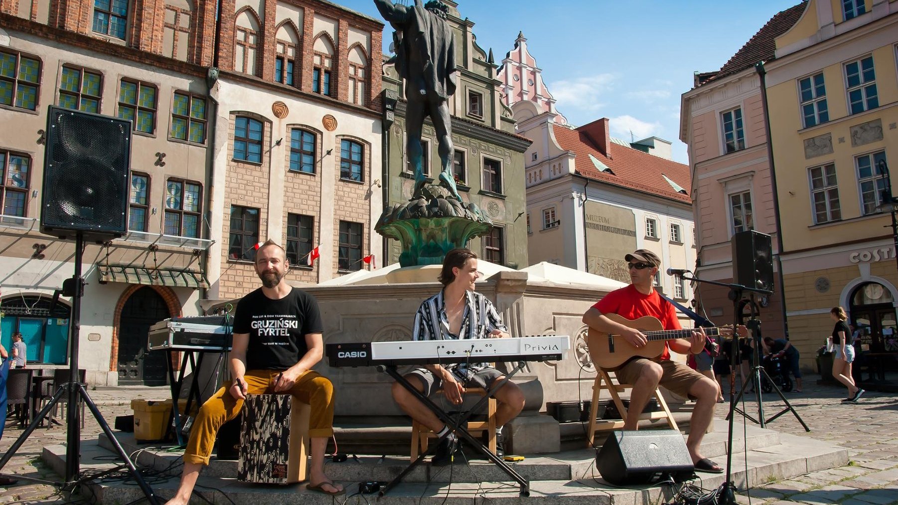 Na zdjęciu zespół grający na instrumentach przed fontanną na Starym Rynku w Poznaniu