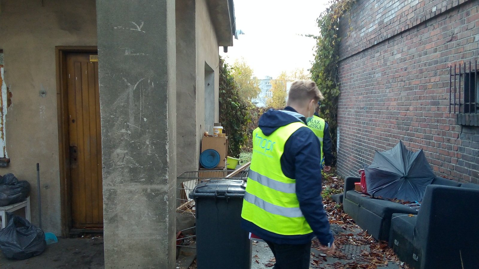 Na zdjęciu osoba w kamizelce z napisem MOPR znajduje się w jednym z koczowisk osób bezdomnych