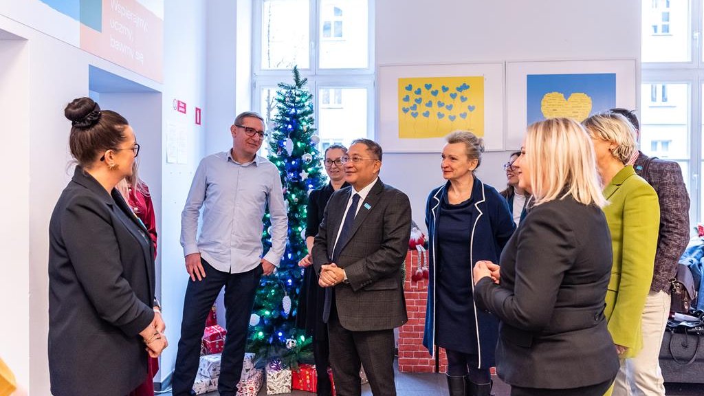 Na zdjęciu grupa ludzi zebrana w dużej sali, w tle choinka i obrazki w barwach ukraińskiej flagi