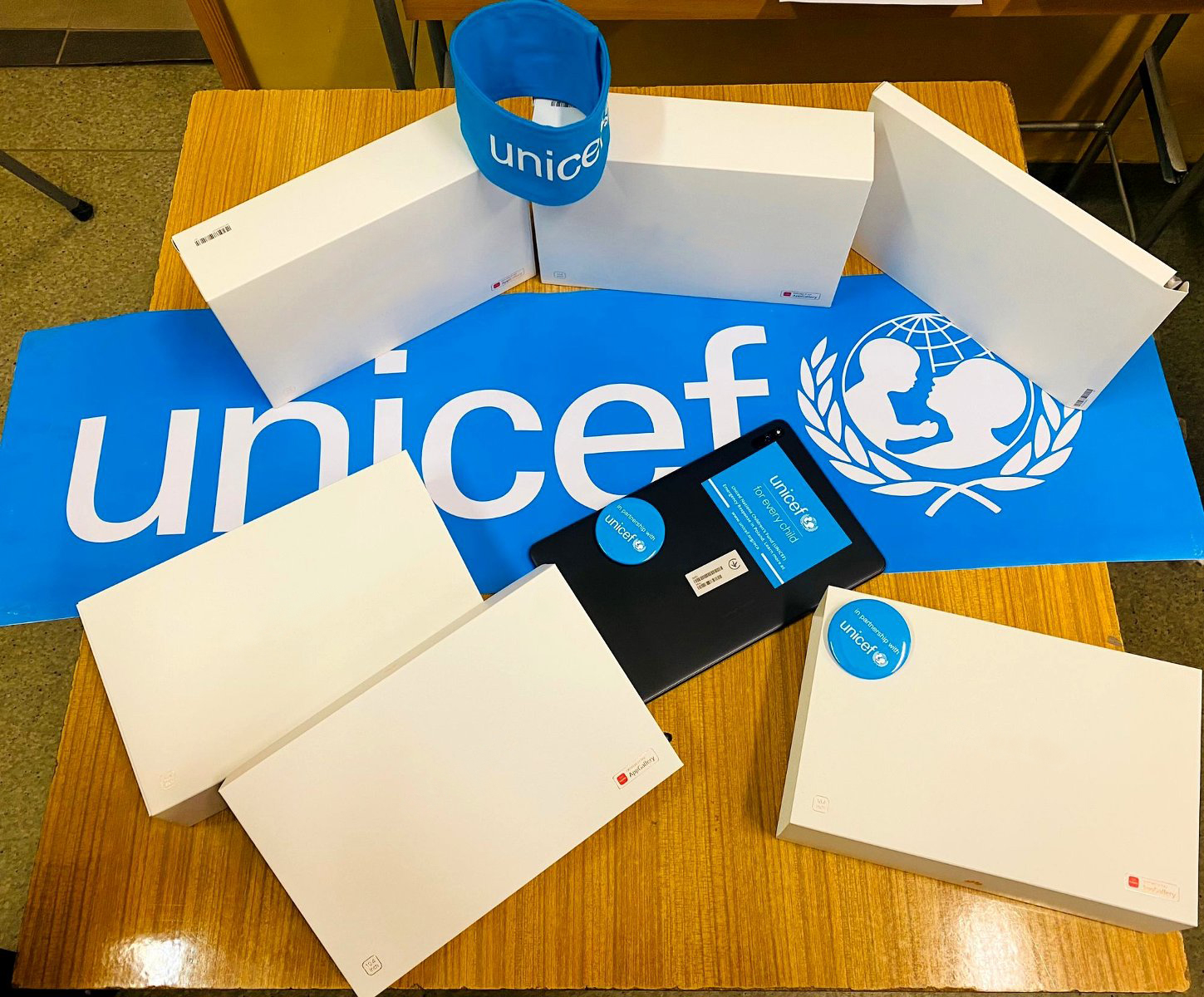 Na zdjęciu tablety - większość w pudełkach - leżące na na stole, obok logo UNICEF - grafika artykułu