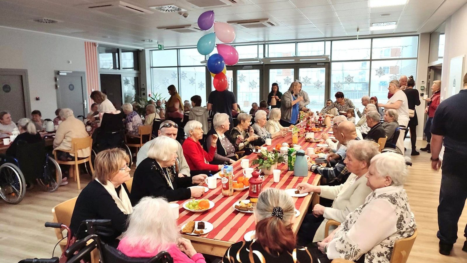 Na zdjęciu duża grupa seniorów i seniorek siedzących przy stołach