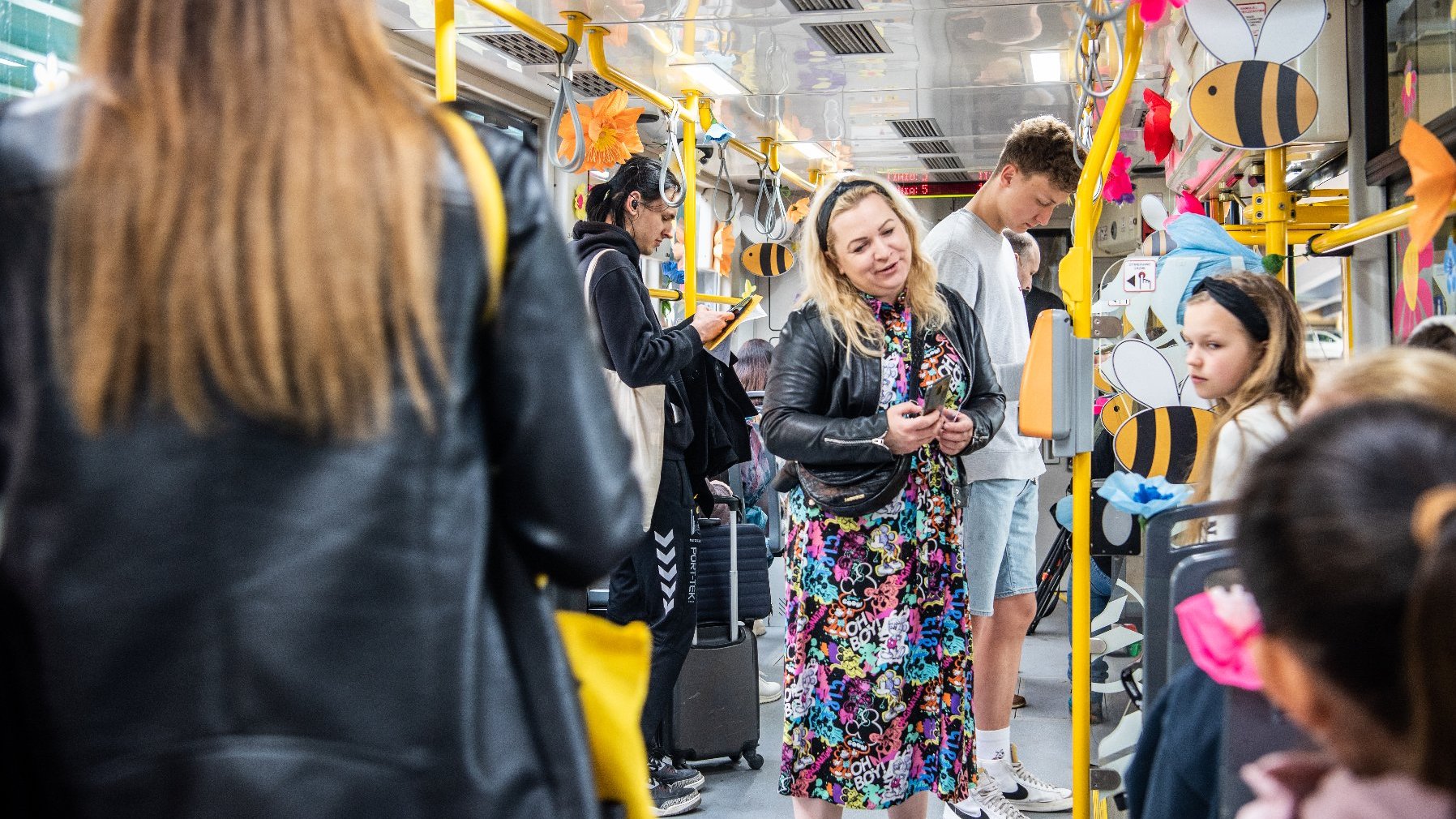 Na zdjeciu wnętrze tramwaju ozdobionego kwiatami, w nim pasażerowie