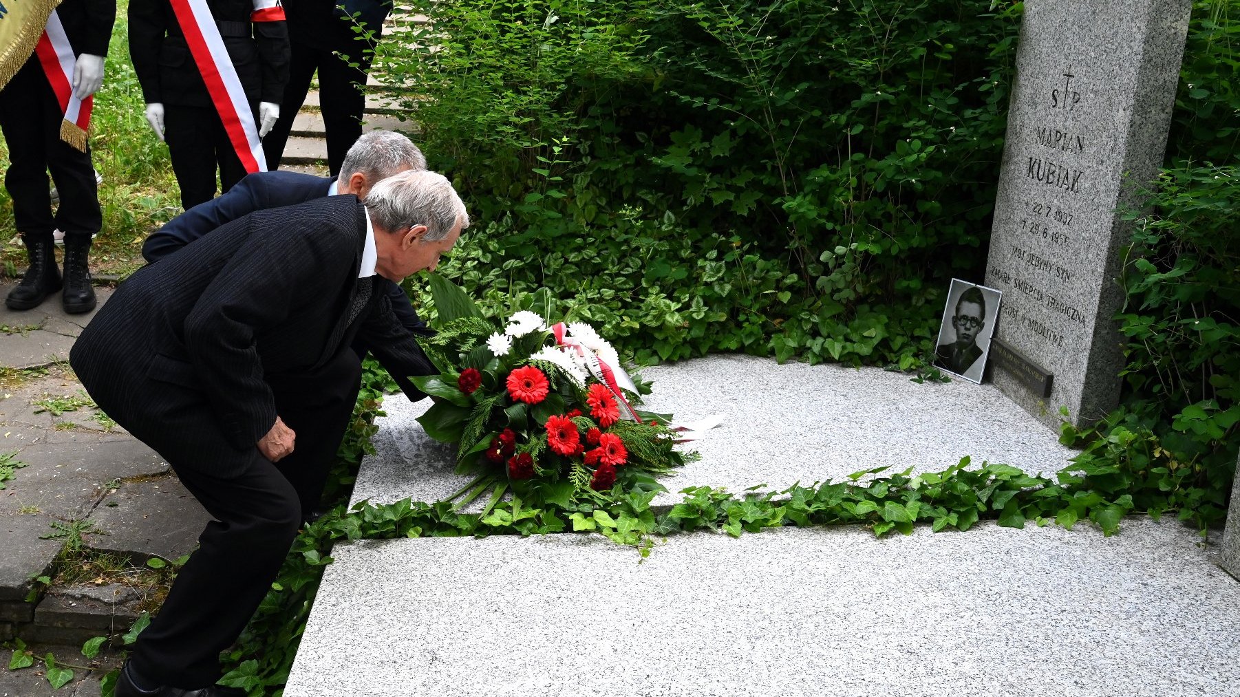 Na zdjęciu dwaj mężczyźni składają kwiaty na grobie