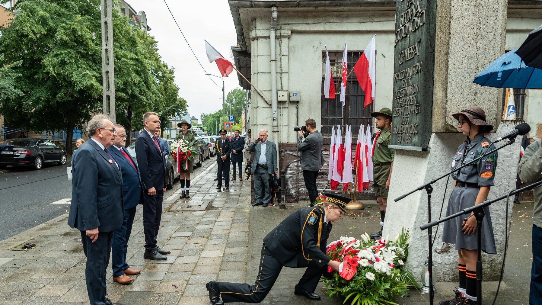 na zdjęciu samorządowcy składający kwiaty pod tablicą, wiązankę składa strażnik miejski