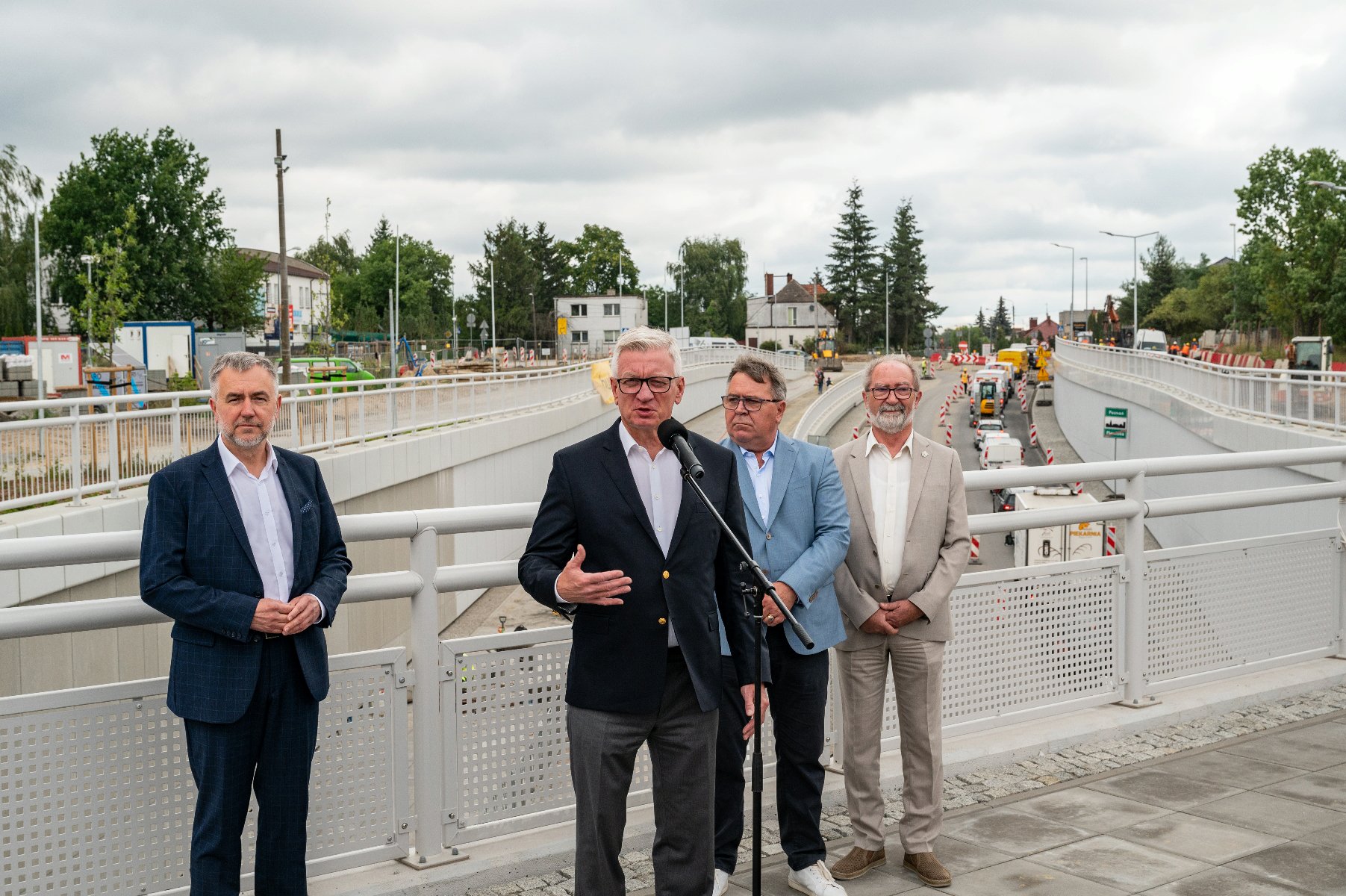 Na zdjęciu czterej mężczyźni, za nimi przejazd pod torami - grafika artykułu