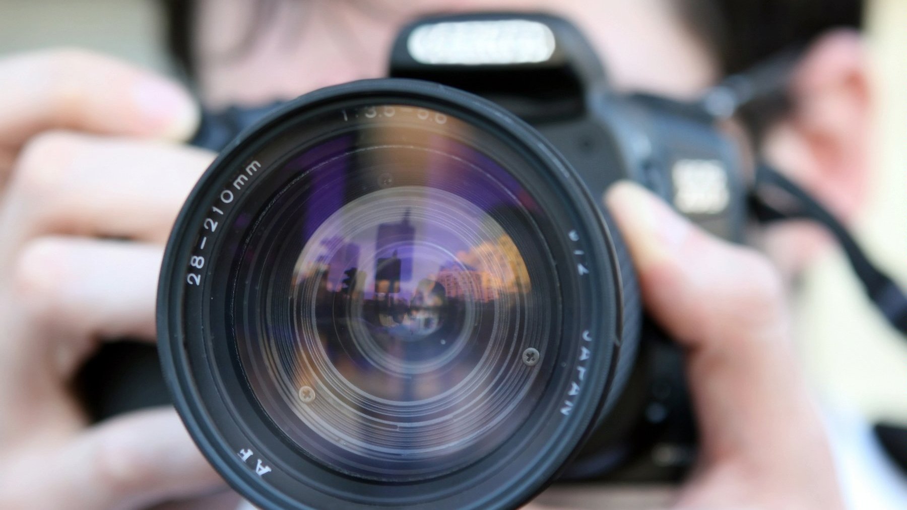 Zdjęcie przedstawia osobę przykładającą do oka aparat fotograficzny.