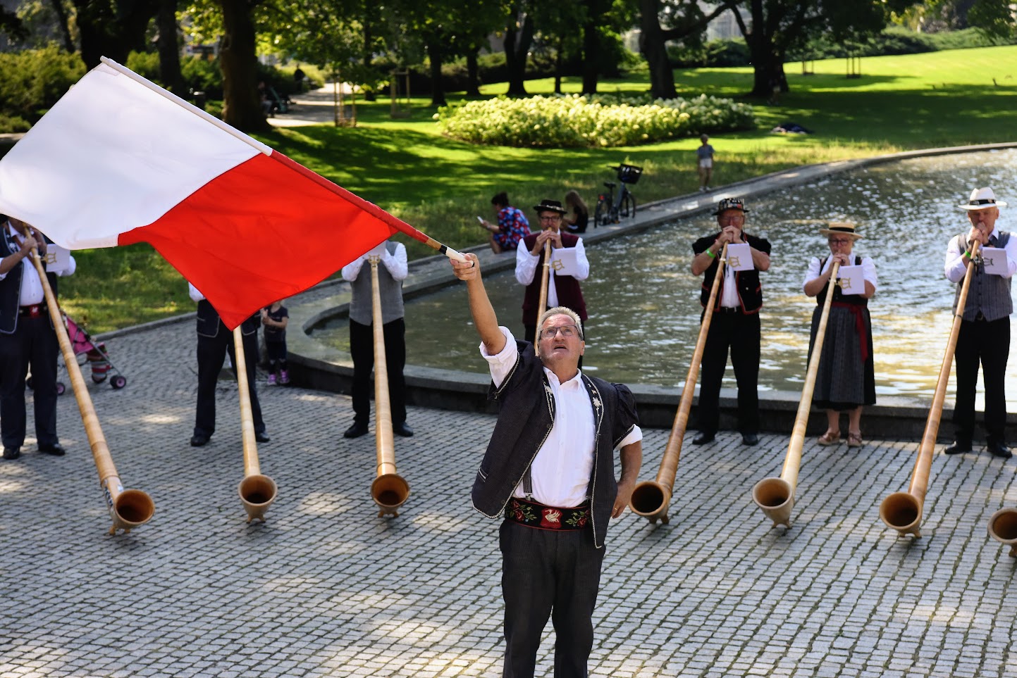 Na zdjęciu mężczyzna z flagą Polski, za nim muzycy grający na rogach - grafika artykułu