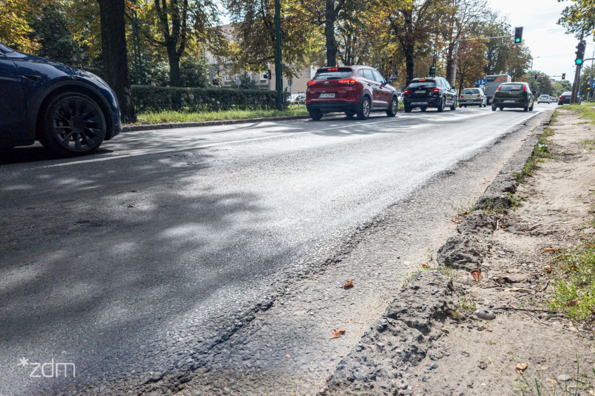 Zniszczona nawierzchnia ul. Reymonta i jadące po niej samochody - grafika artykułu