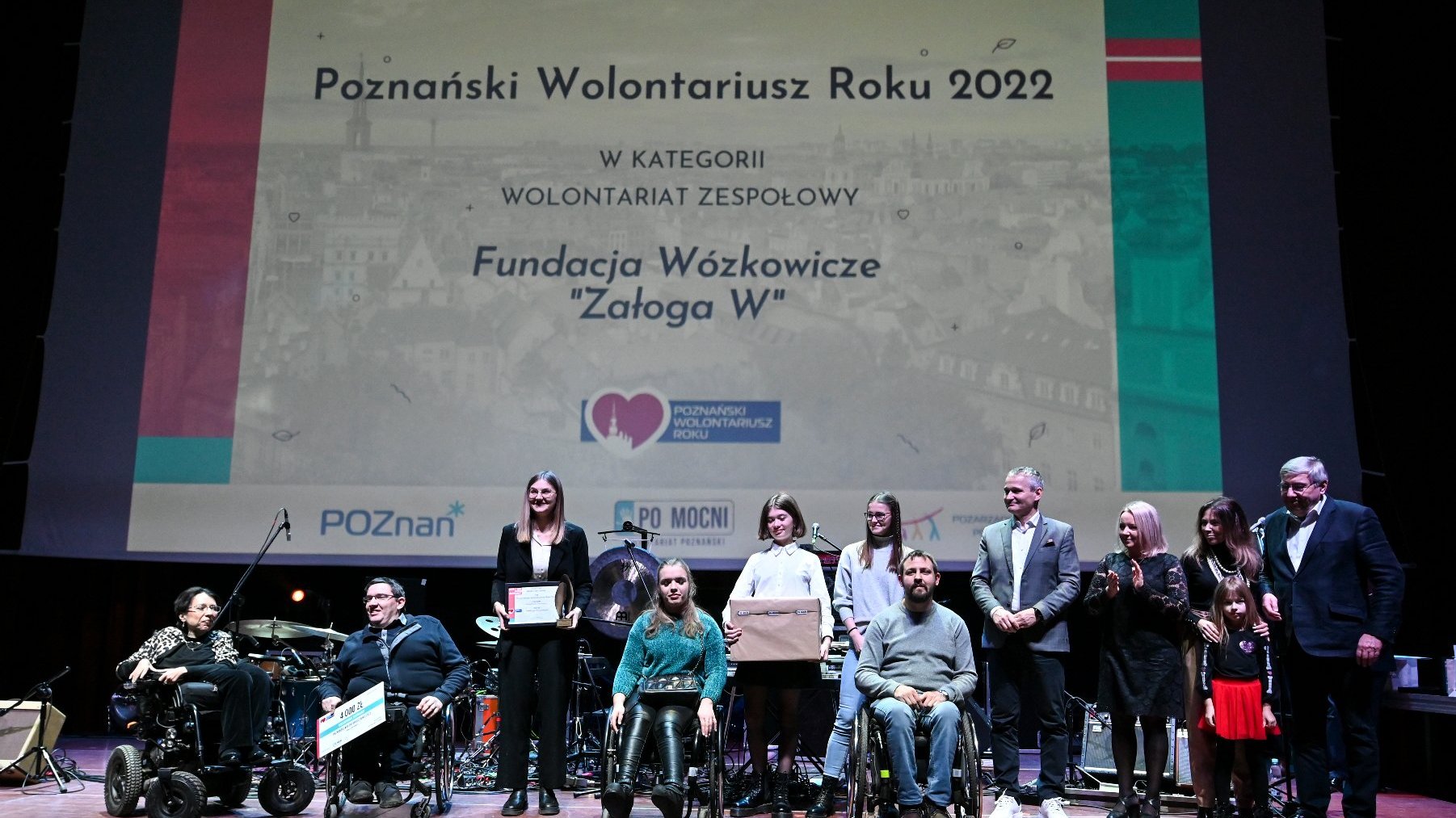 Na zdjęciu widąć zdobywców statuetki w kategorii Wolontariat Zespołowy - "Załogę W", czyli wolontariuszy Fundacji Wózkowicze. Na scenie nagrodę wręczają im: Grzegorz Ganowicz, przewodniczący rady miasta, Jędrzej Solarski, zastępca prezydenta Poznania, Monika Danelska, miejska radna oraz Magdalena Pietrusik-Adamska, dyrektorka Wydziału Zdrowia i Spraw Społecznych UMP.