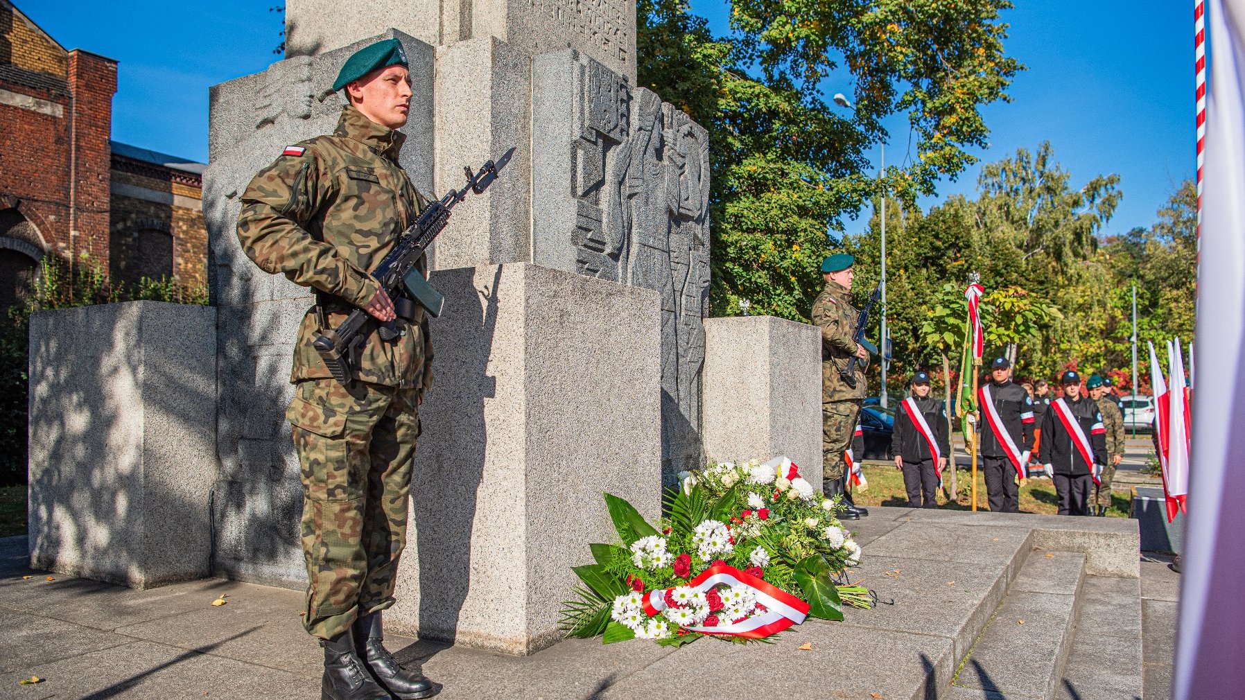 Na zdjęciu żołnierz pełniący wartę przy pomniku, pod pomnikiem leżą kwiaty