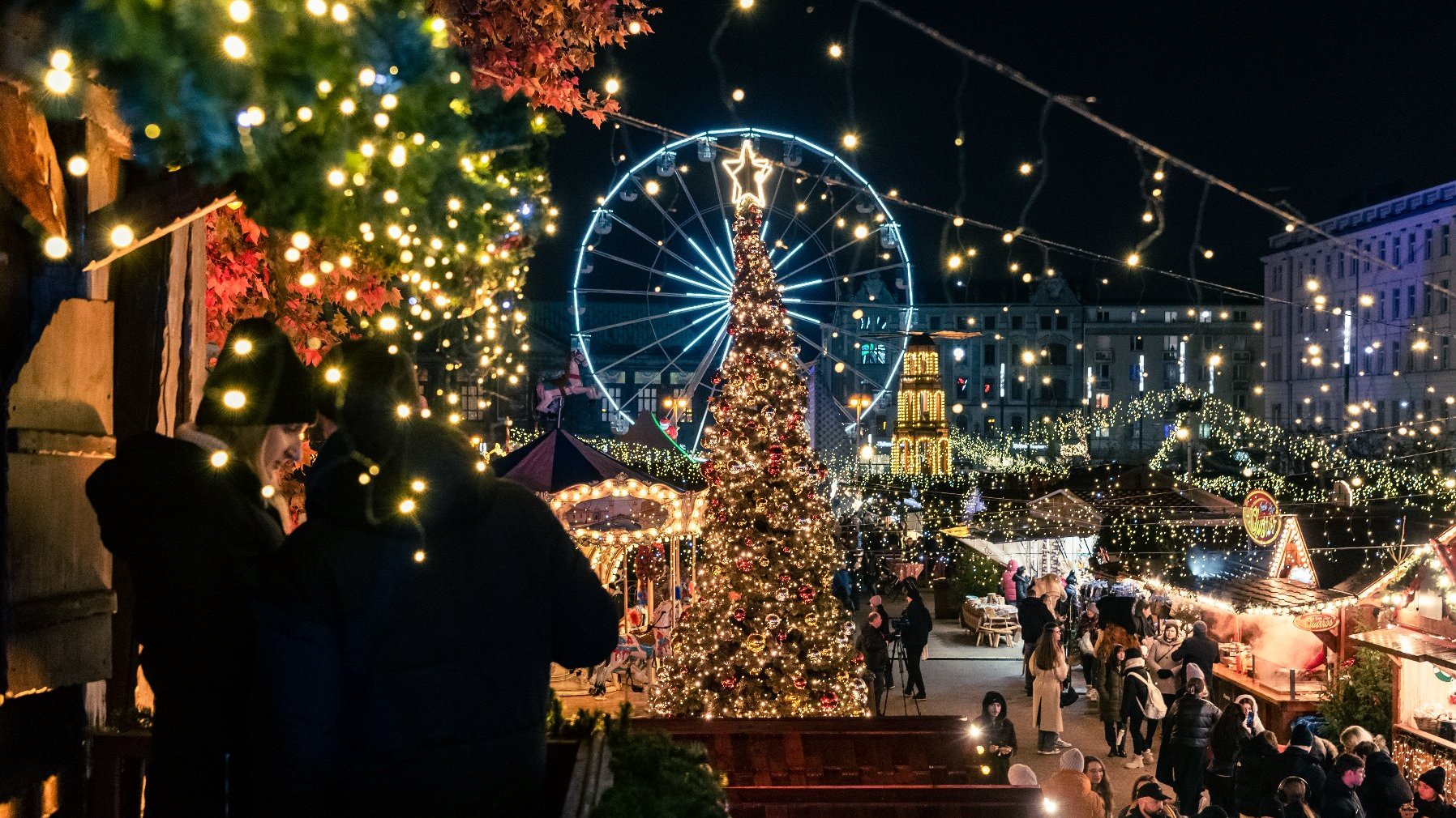 Zdjęcie przedstawia jarmark na placu Wolności. Widać na nim budki wystawiennicze, tłum ludzi i młyńskie koło.