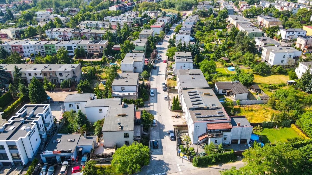 Zdjęcie przedstawia widok na budynki jednorodzinne, zieleń i drogi z lotu ptaka.