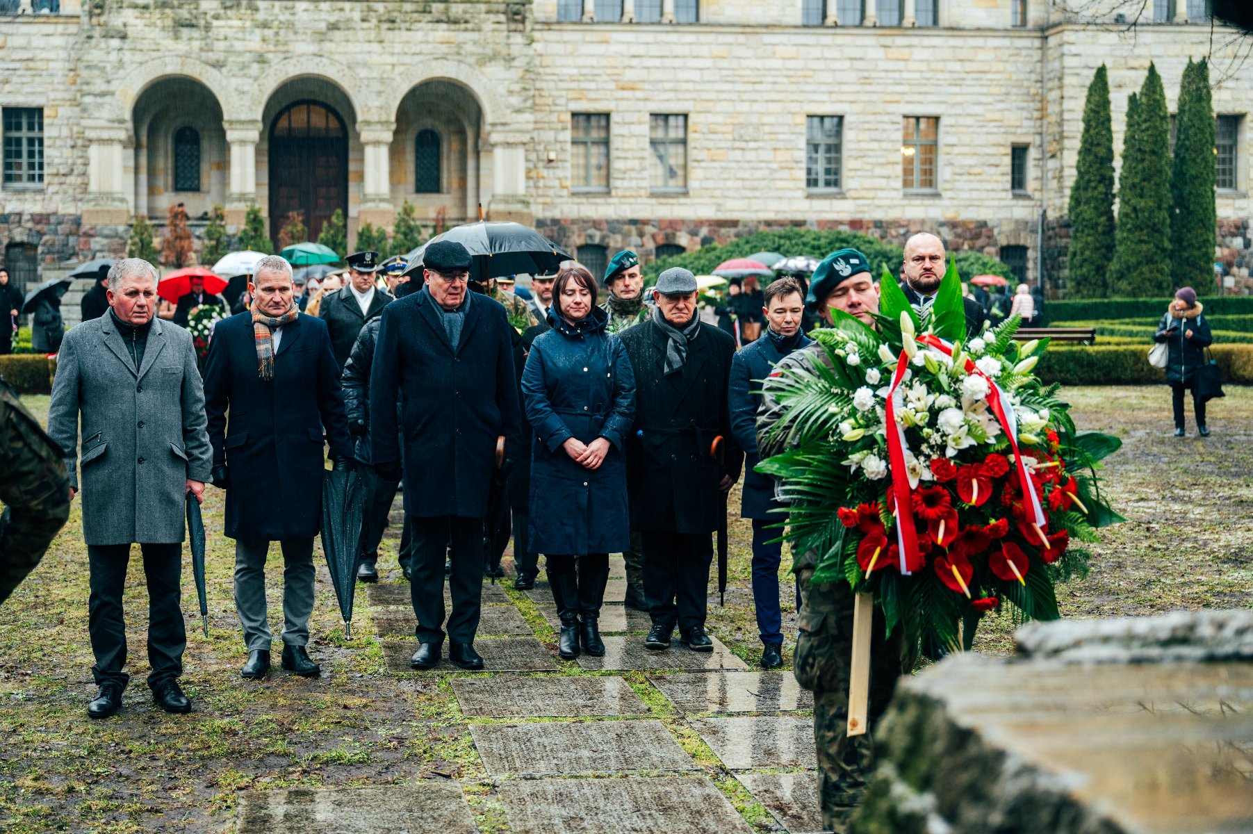 Na zdjęciu przedstawiciele władz rządowych i samorządowych stoją przed pomnikiem, przed nimi strażnik trzymający wiązankę - grafika artykułu