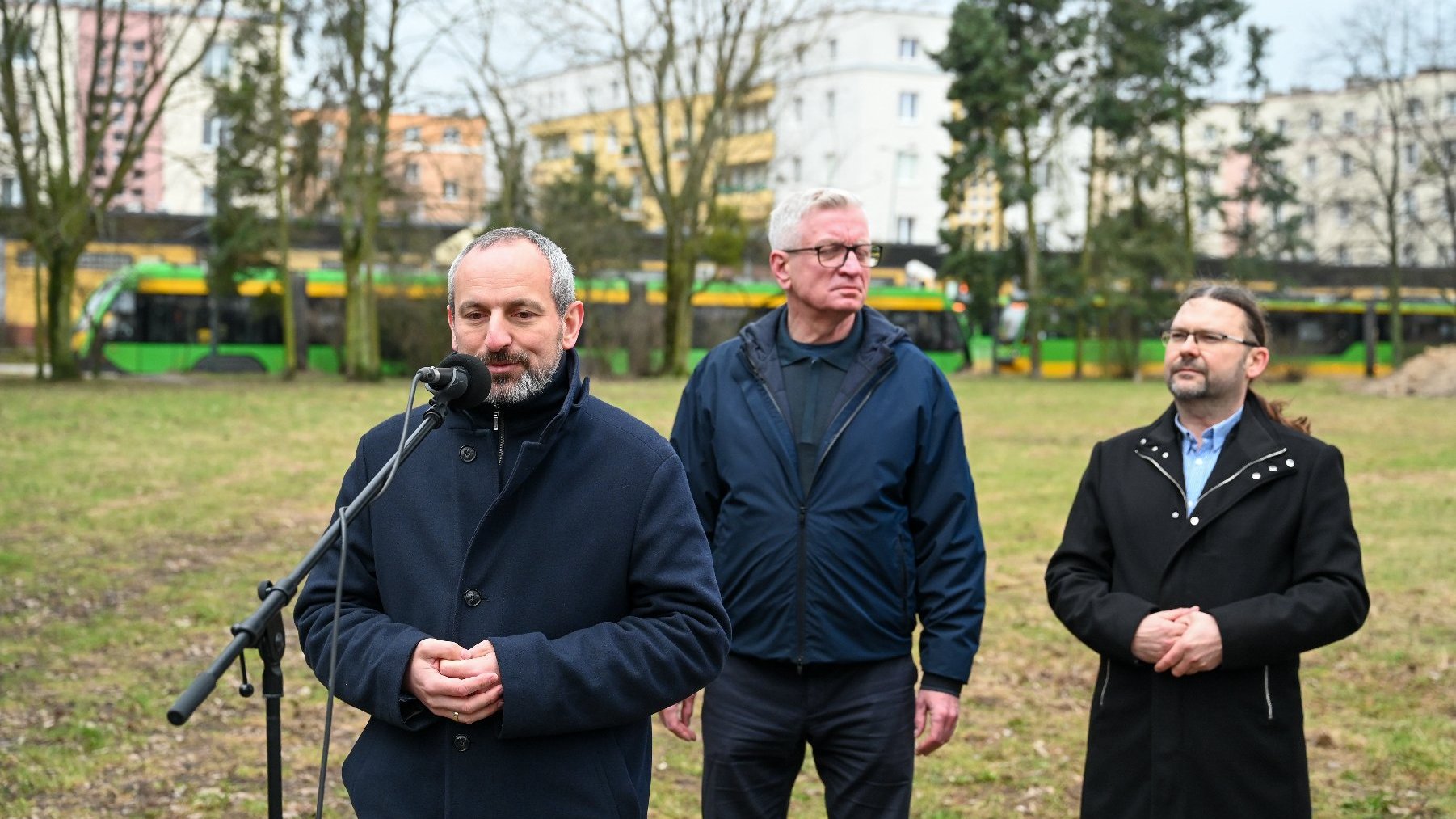 Na zdjęciu trzech mężczyzn na pętli ogrody, jeden z nich przy mikrofonie