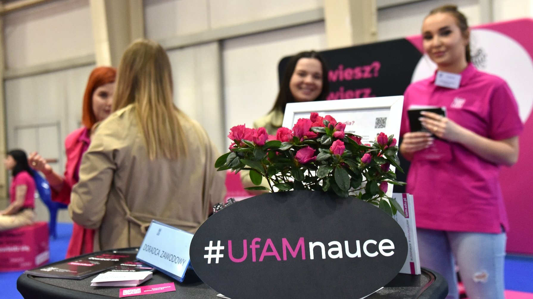 Na zdjęciu stolik z kwiatami i napisem: ufam nauce, w tle młode kobiety