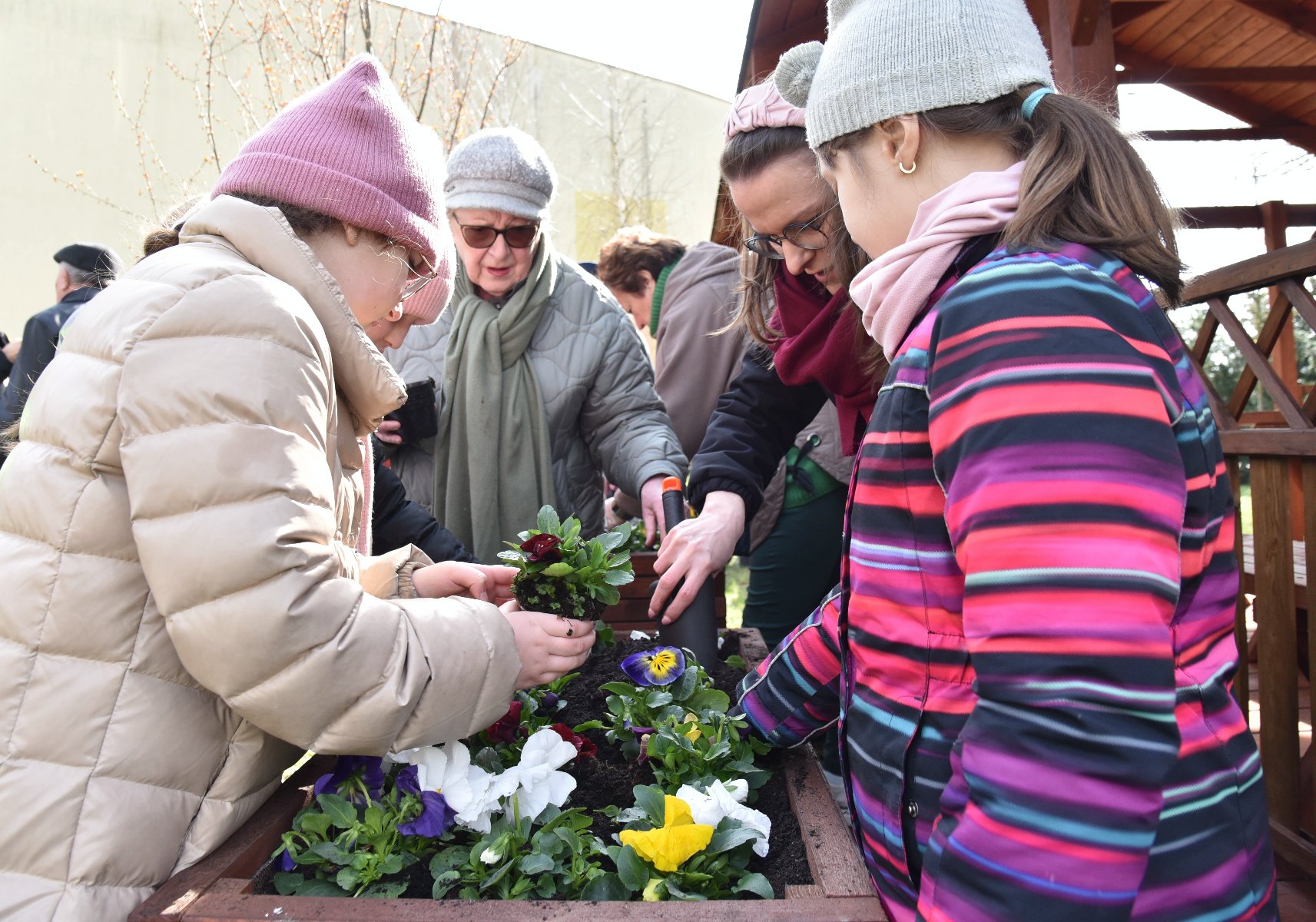 Zdjęcie przedstawia dzieci i dorosłych sadzących rosliny. - grafika artykułu