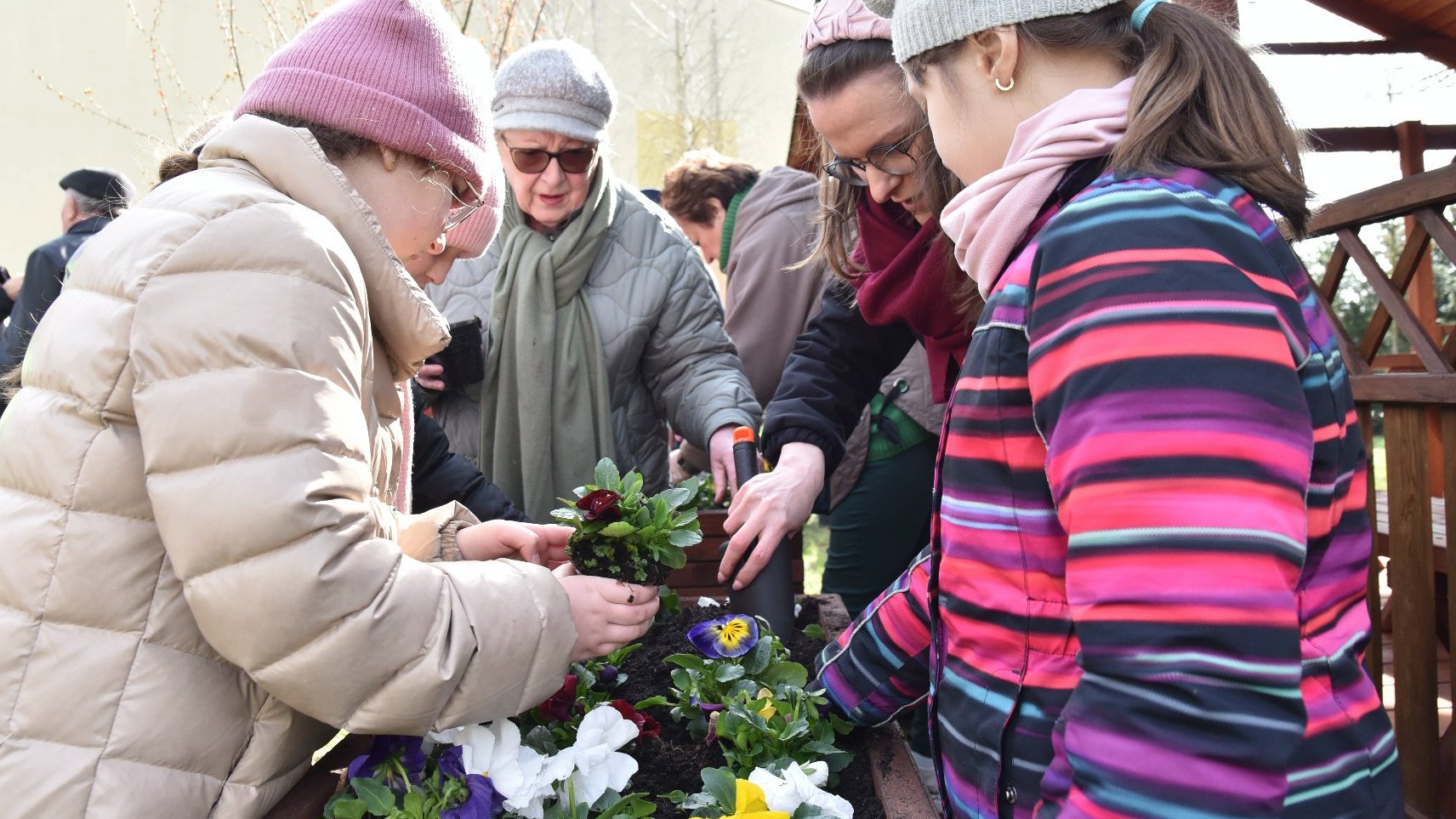 Zdjęcie przedstawia dzieci i dorosłych sadzących rosliny.