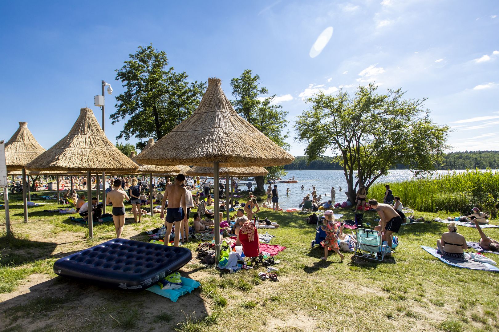 Zdjęcie przedstawia plażę, na kórej odpoczywają ludzie. W tle widać jezioro. - grafika artykułu