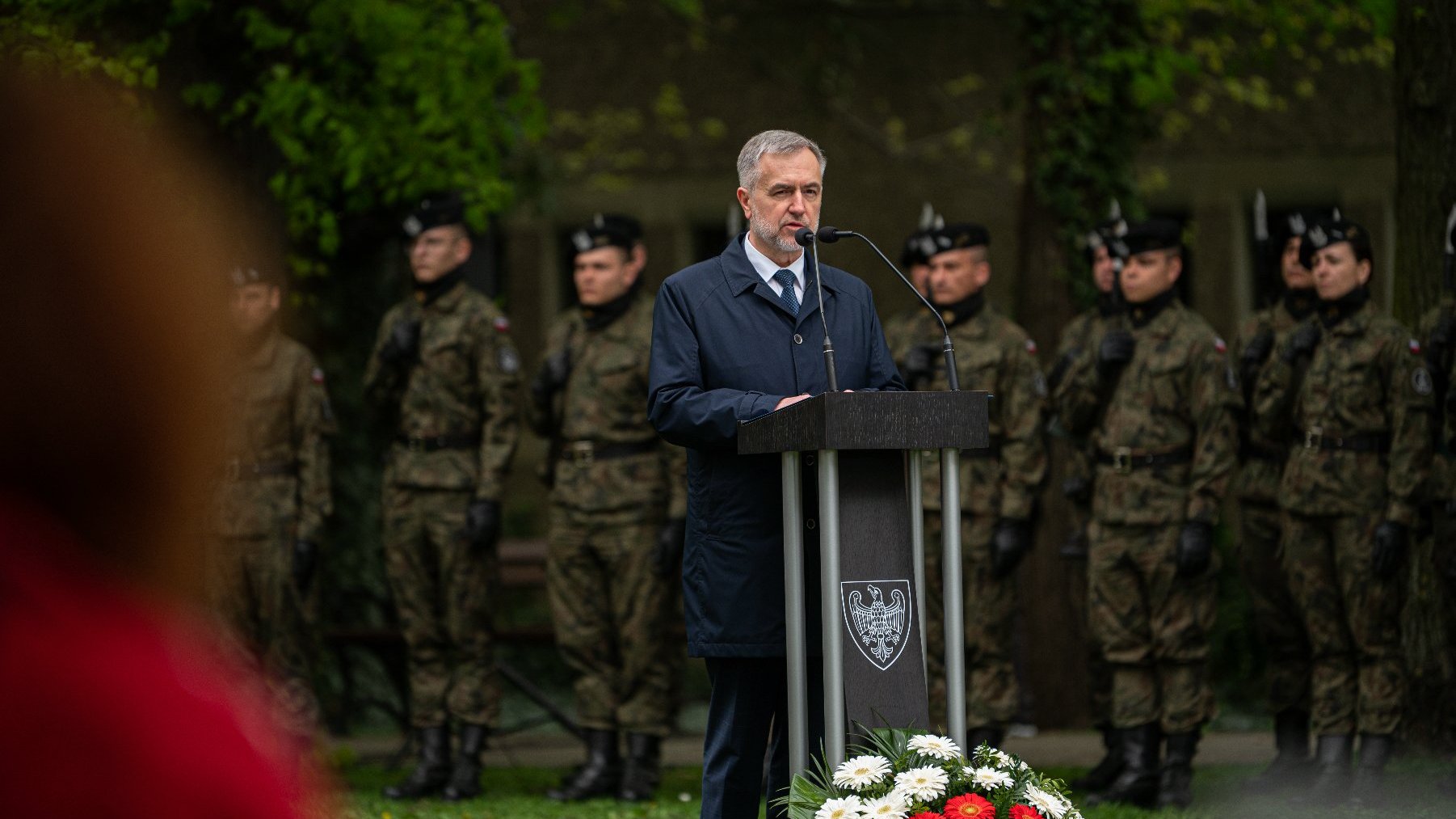 Na zdjęciu marszałek województwa za mównicą, w tle stoją żołnierze