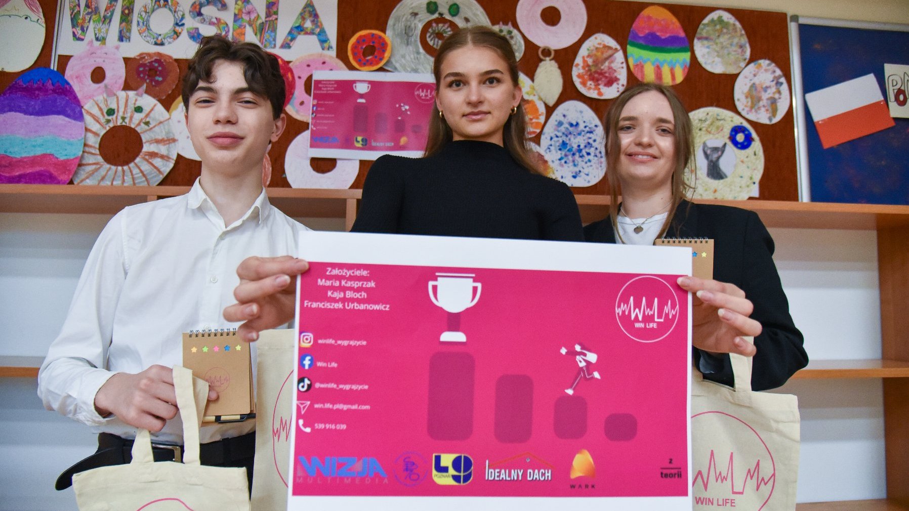 Na zdjęciu troje uczniów trzymających przed sobą różowy plakat