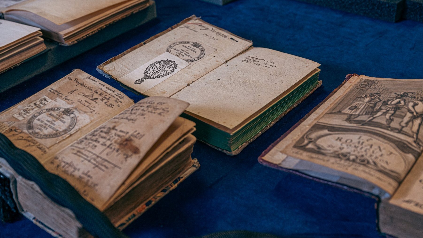 Na zdjęciu trzy stare ksiażki, otwarte, leżące na stole