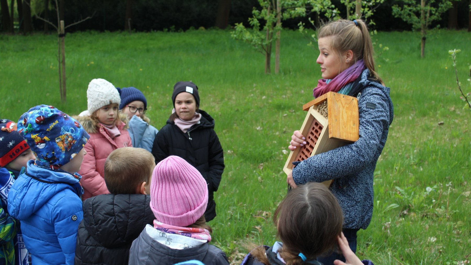 Zdjęcie przedstawia grupę dzieci i kobietę trzymającą domek dla owadów.