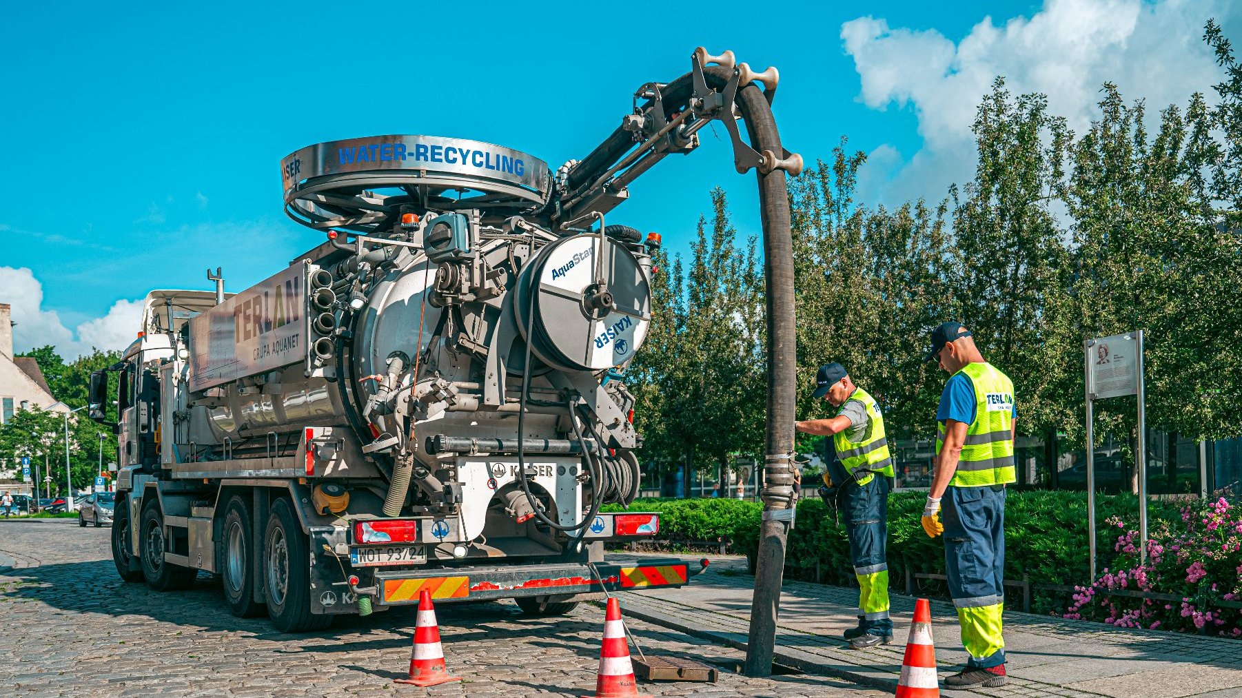 Zdjęcie przedstawia spacjalistyczny samochód oraz pracowników podczas czyszczenia studzienek kanalizacyjnych.