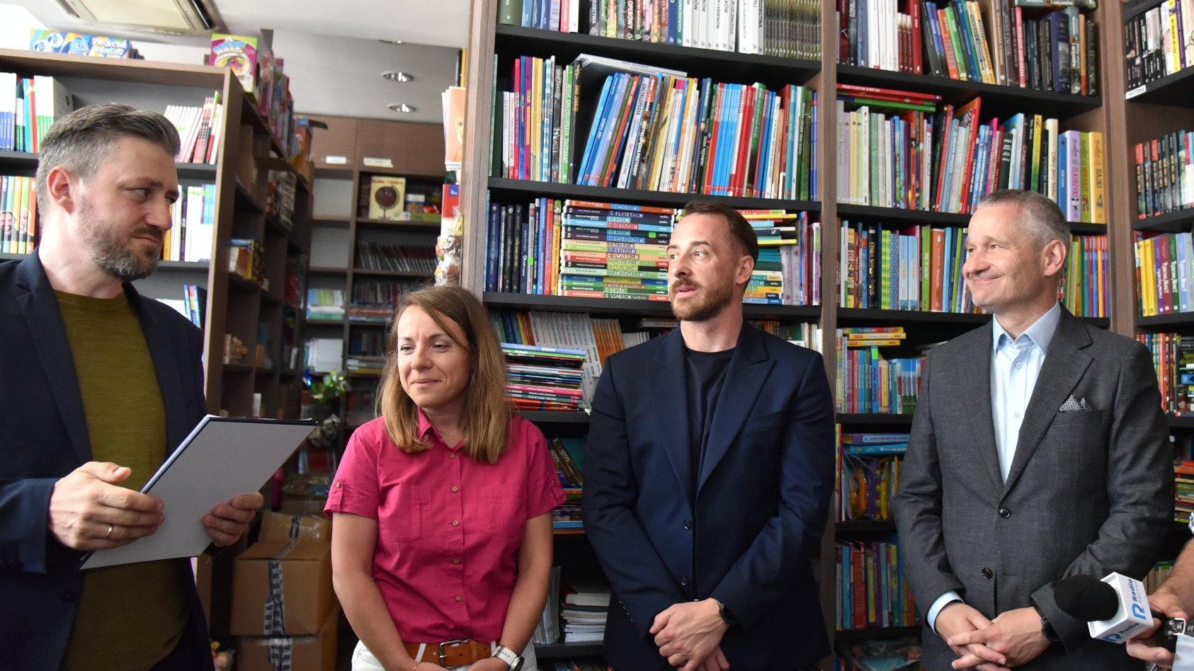 Zdjęcie przedstawia trzech mężczyzn i jedną kobietę stojących przed półką z książkami.