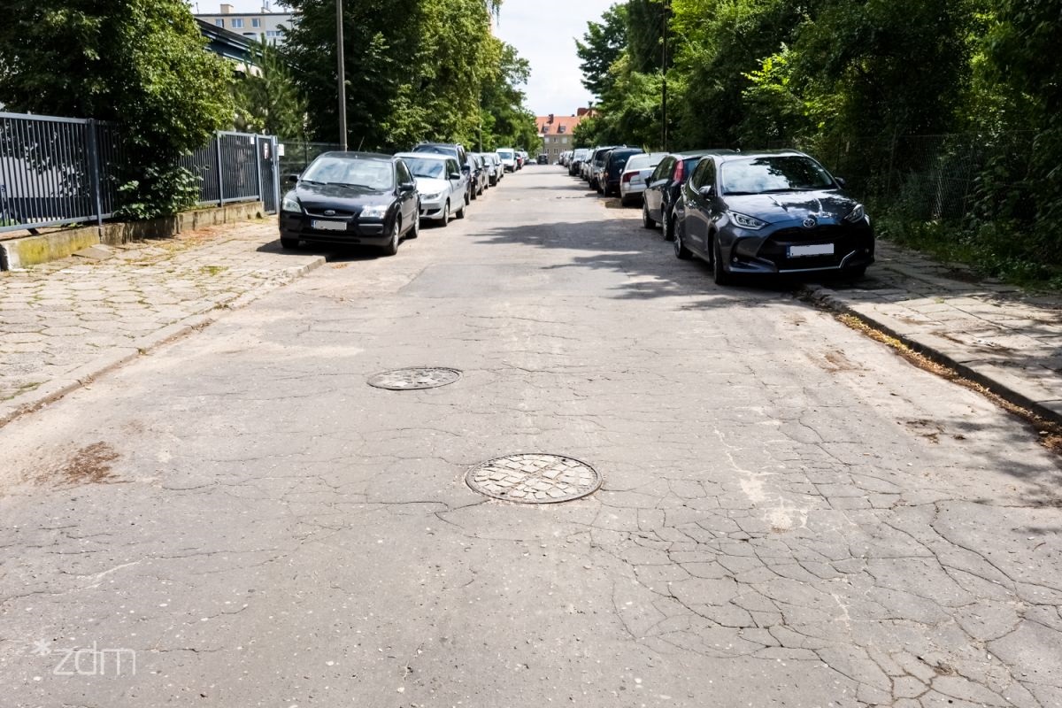 Zdjęcie przedstawia ulicę. Po jej obu stronach stoją zaparkowane samochody. - grafika artykułu
