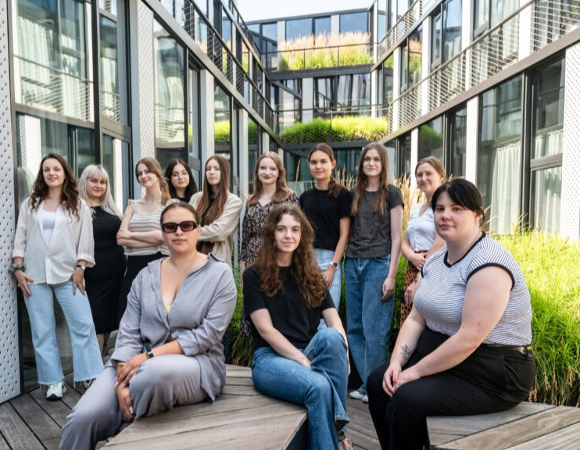 Program Uniwersytetu Sukcesu to bezpłatna inicjatywa skierowana do młodych kobiet w wieku 18-25 lat Grupa kobiet w wieku 18-25 lat pozuje do zdjęcia na tarasie w nowoczesnym budynku.