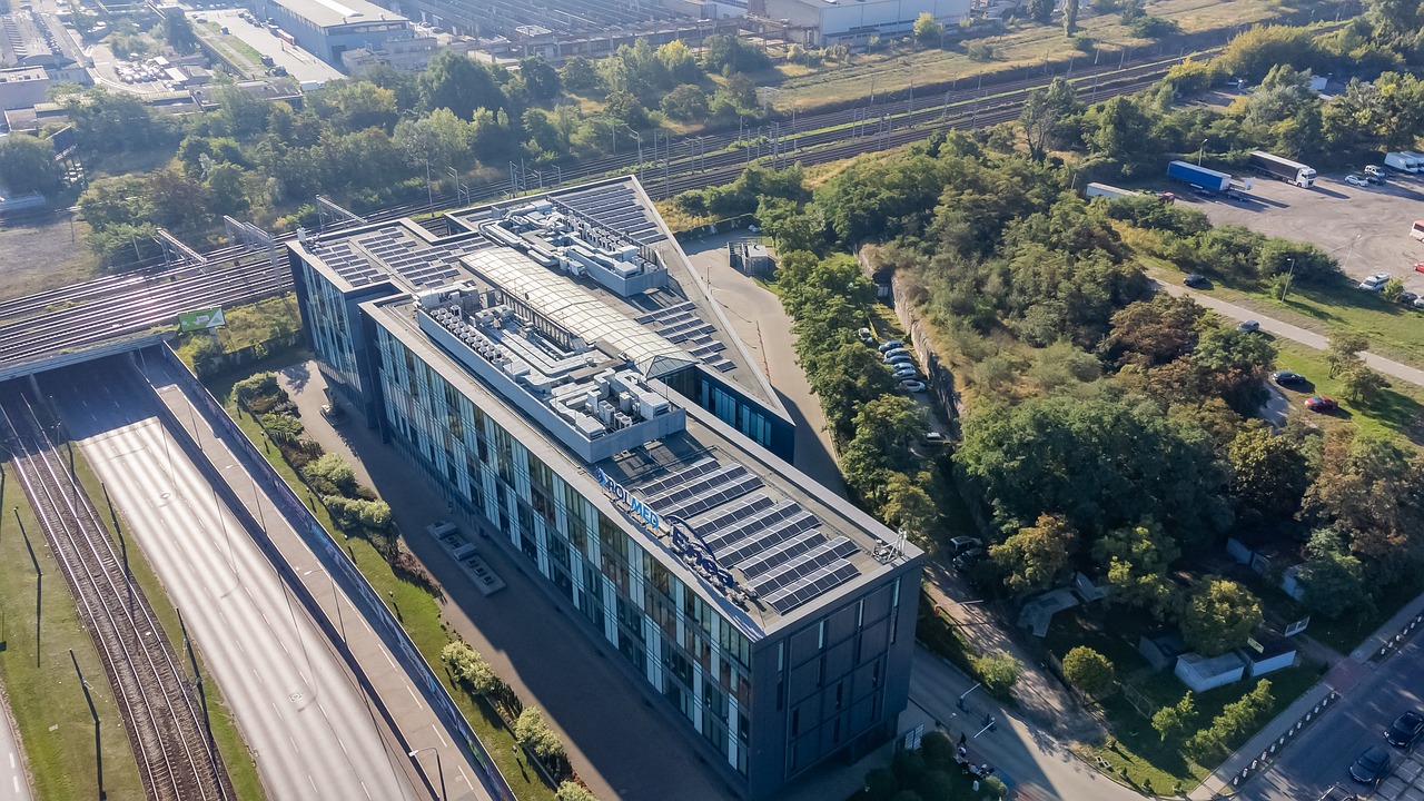 Zdjęcie zostało zrobione z lotu ptaka. W środku kadru znajduje się biurowiec Skalar Office Center widoczny od góry. Za budynkiem widać tory kolejowe. Z lewej strony widać ulicę Hetmańską oraz tory tramwajowe. Z prawej strony budynku widać zadrzewiony teren oraz plac parkingowy. - grafika artykułu