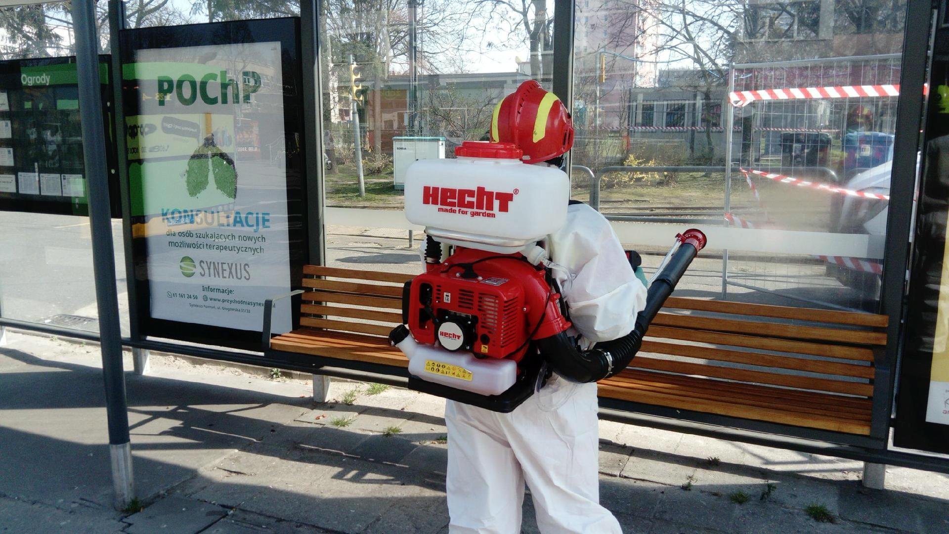 Stojący tyłem człowiek w białym kombinezonie ochronnym dezynfekuje przystanek w Poznaniu