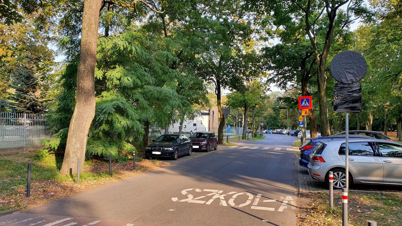 Ul. Za Cytadelą. Próg i napis Szkoła na jezdni. Po obu stronach drogi parkujące auta i drzewa