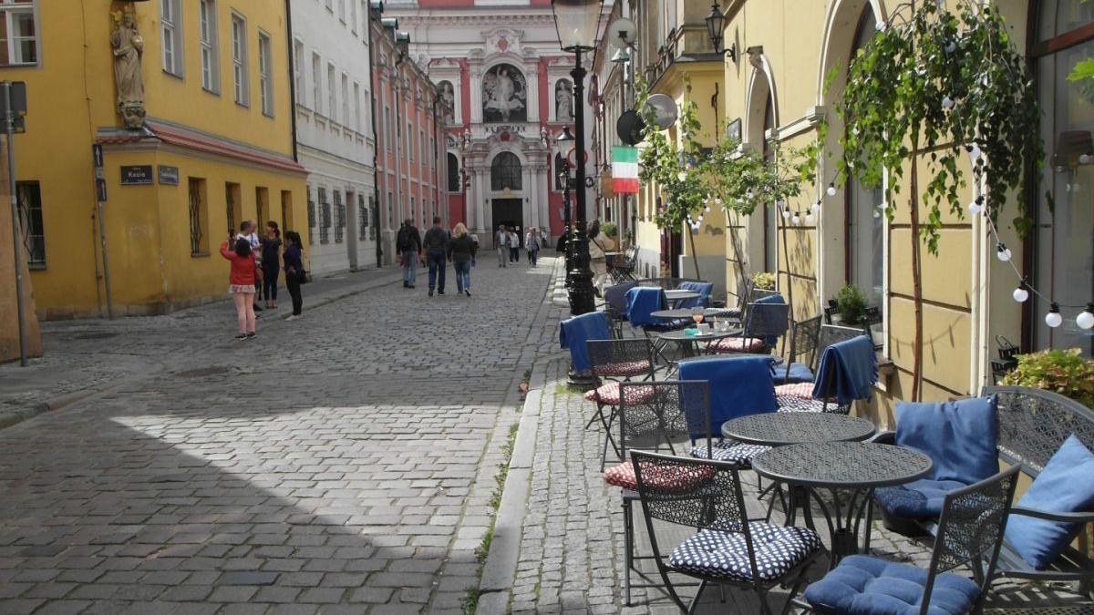 Zdjęcie: na pierwszym planie ogródek gastronomiczny, na krzesłach wiszą niebieskie koce. W tle poznańska fara - grafika artykułu